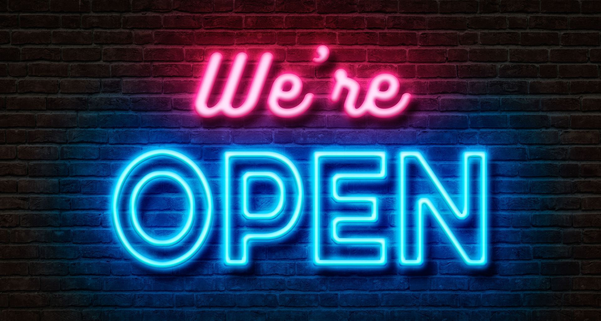 Neon sign reading “We’re OPEN” in pink and blue on a dark brick wall