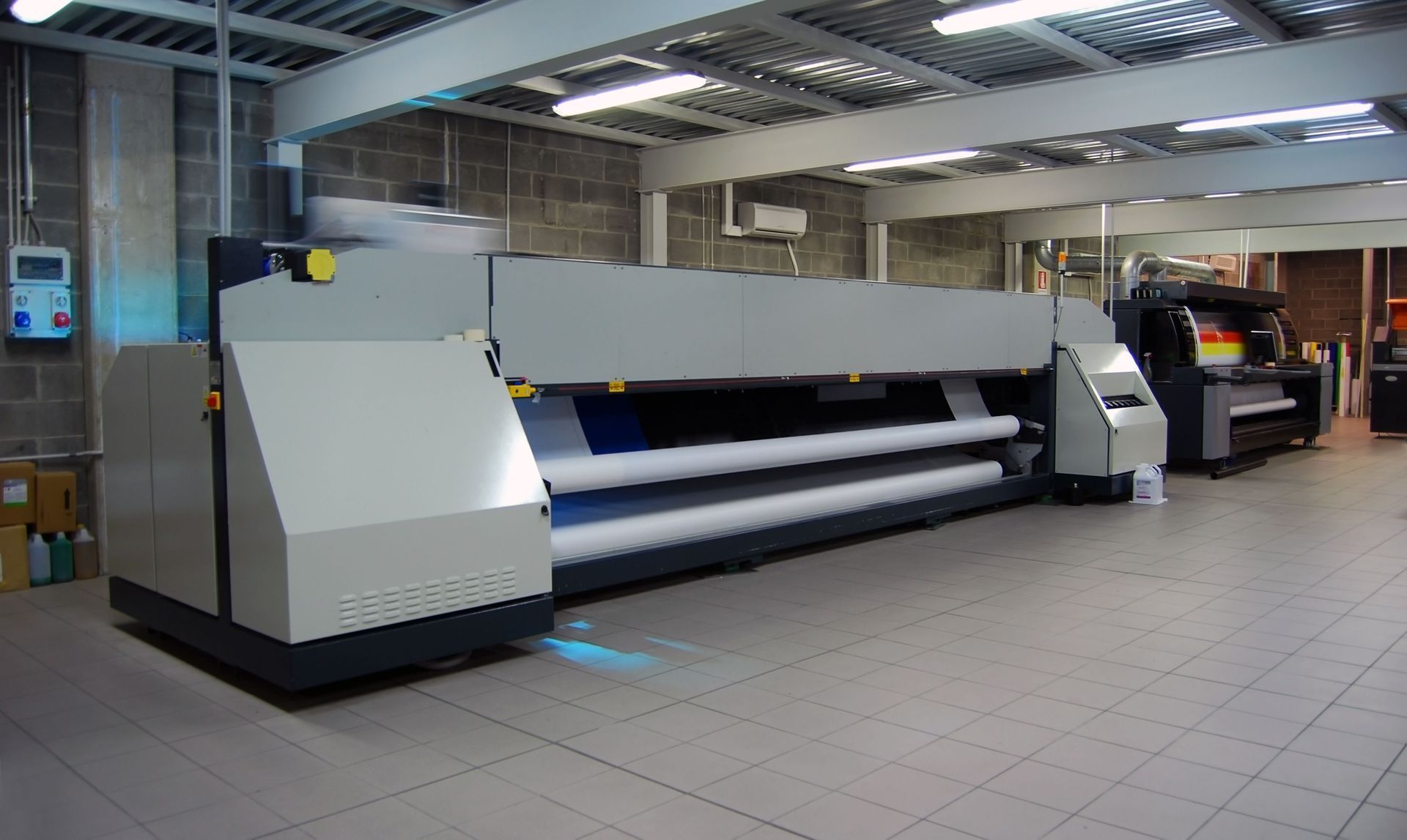 Large industrial printer in a workshop, printing a wide roll of material.