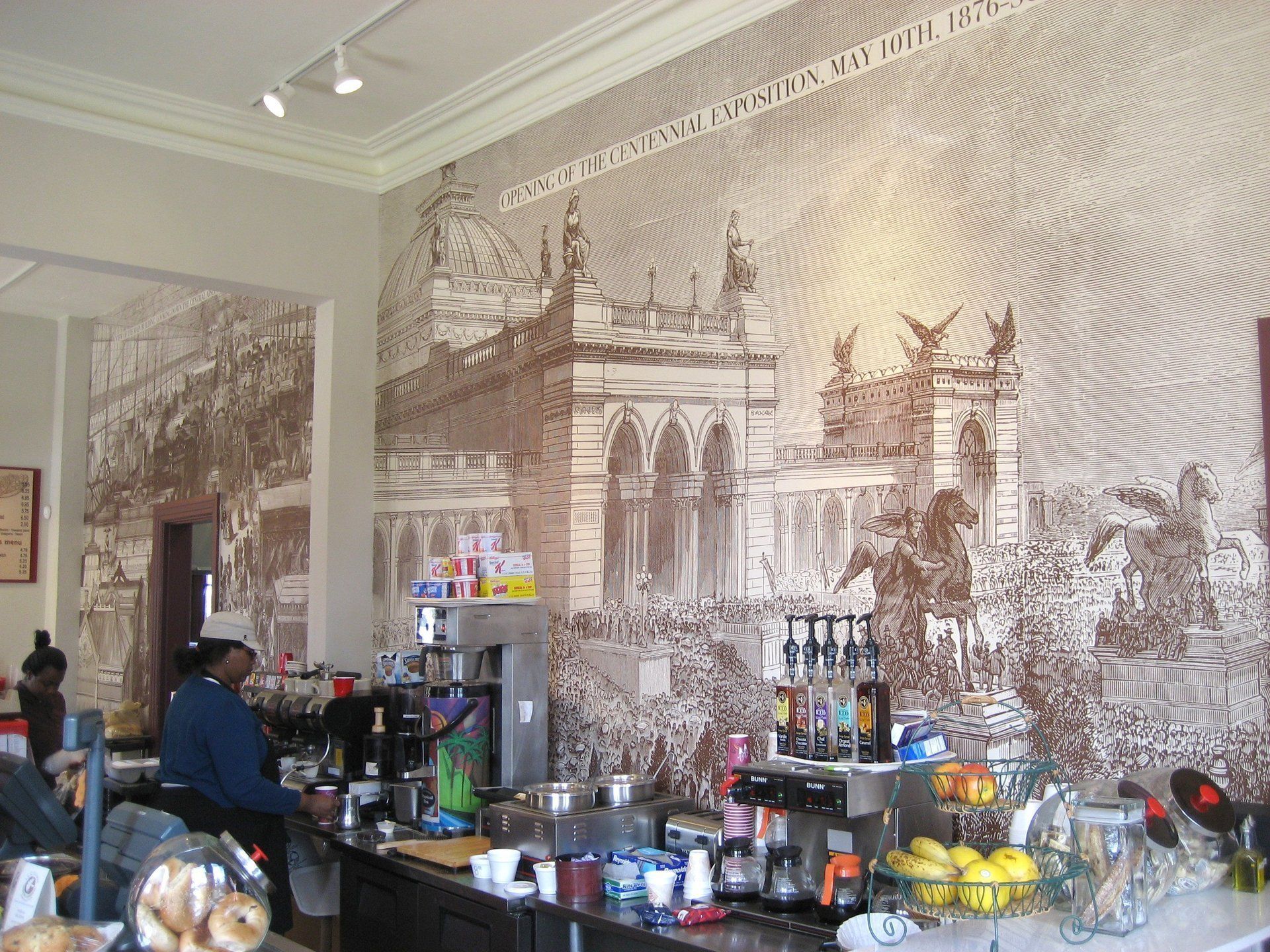 Cafe counter with customers, drinks, and a large sepia mural of a church on the wall