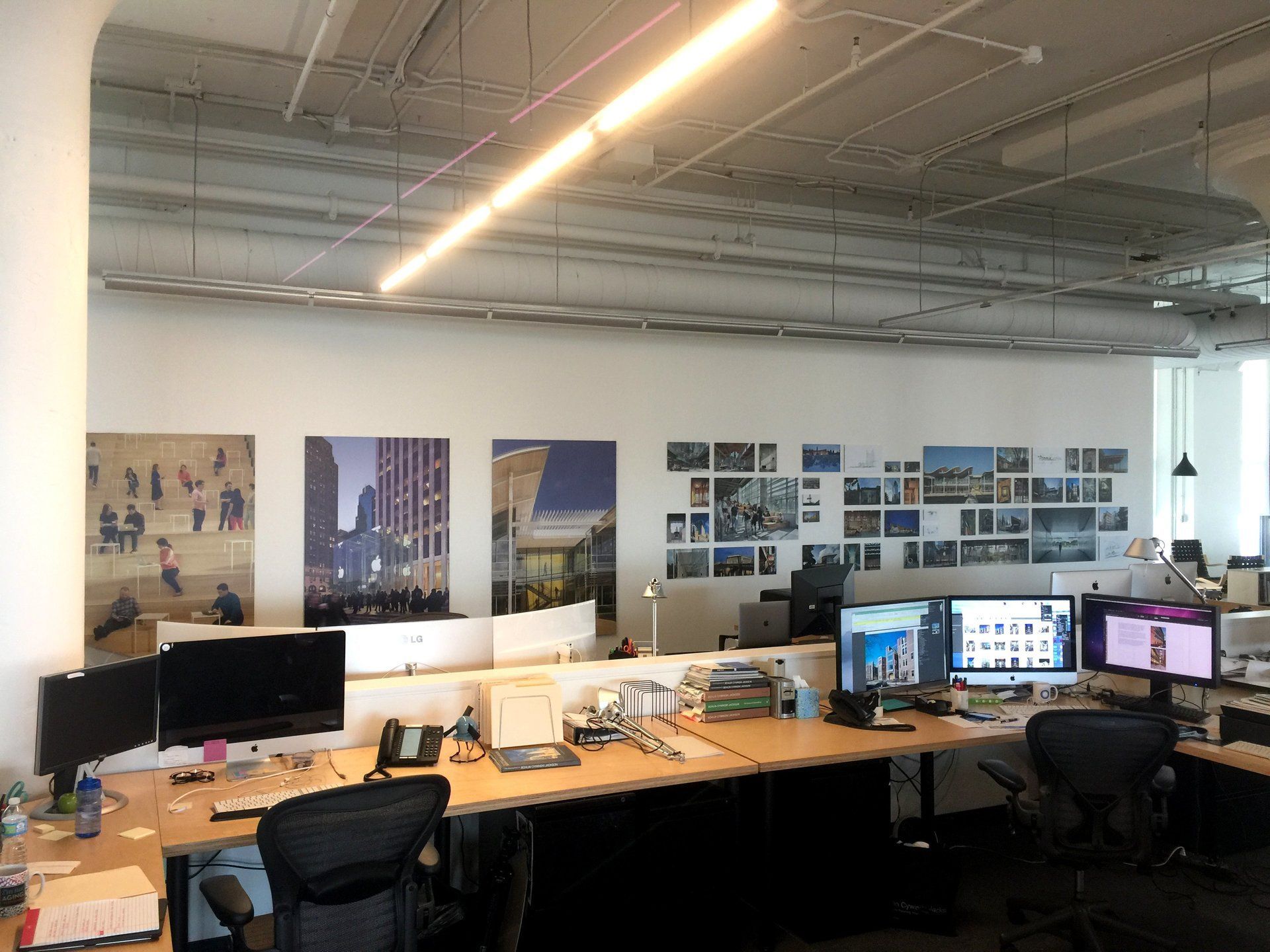 Modern office with desks, dual monitors, wall posters, and exposed ceiling lights