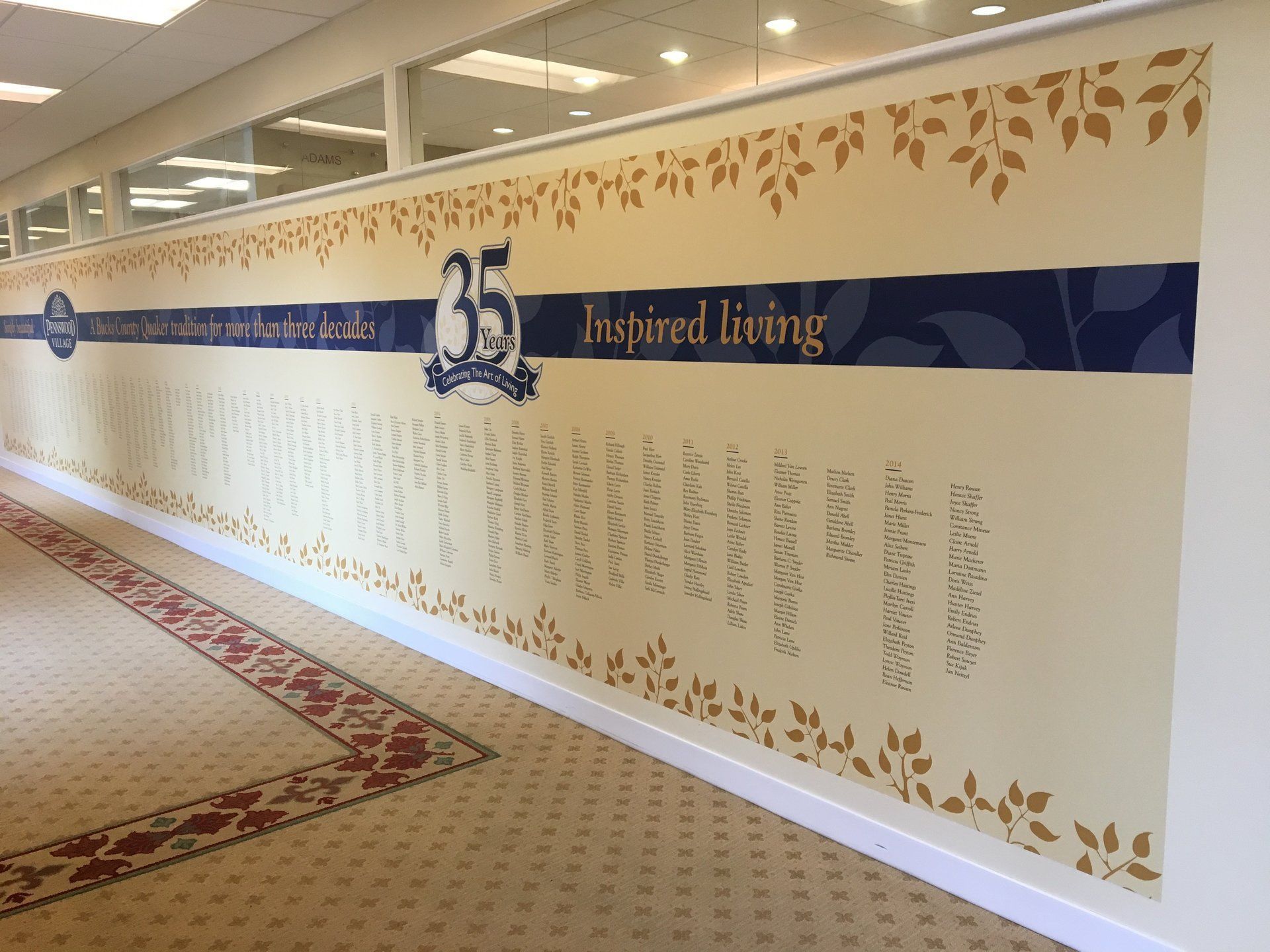 Long hallway wall mural with a blue banner, gold leaf accents, and many handwritten names.