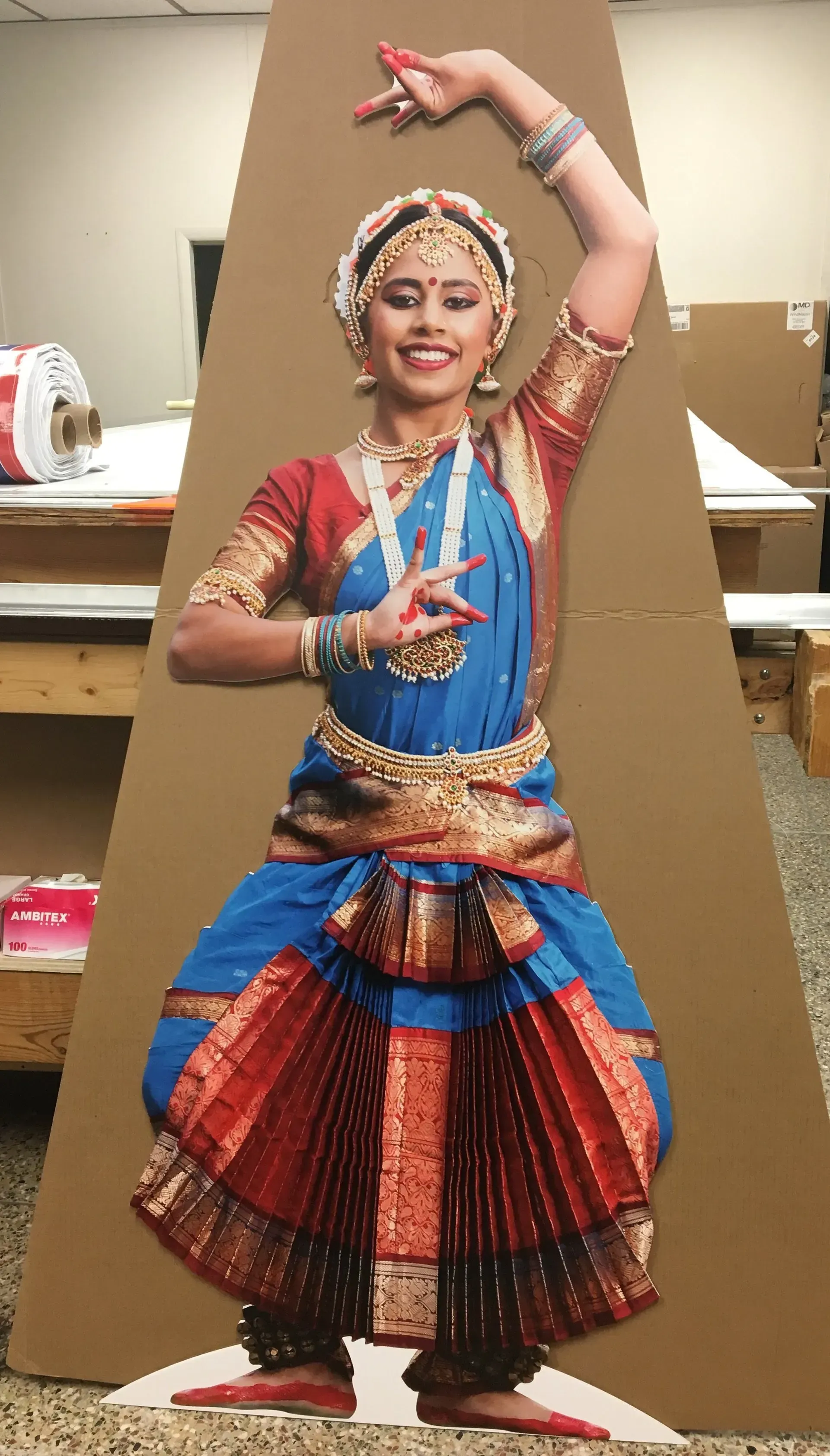 Woman in blue and red classical dance costume posing with raised arms indoors
