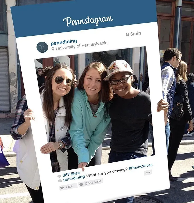 Three smiling students posing in a Penn State Instagram-style photo frame outdoors