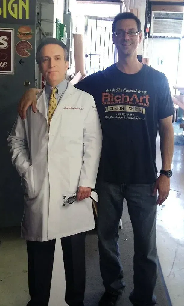 Man standing beside a life-size wax figure in a white lab coat indoors