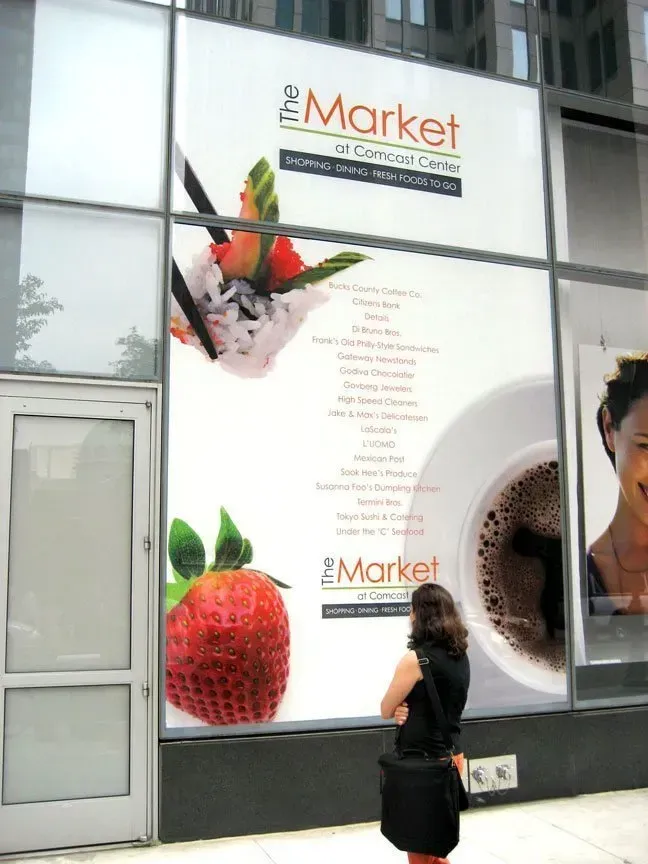 Woman standing outside a storefront window with “the Market” signage and a large strawberry graphic.