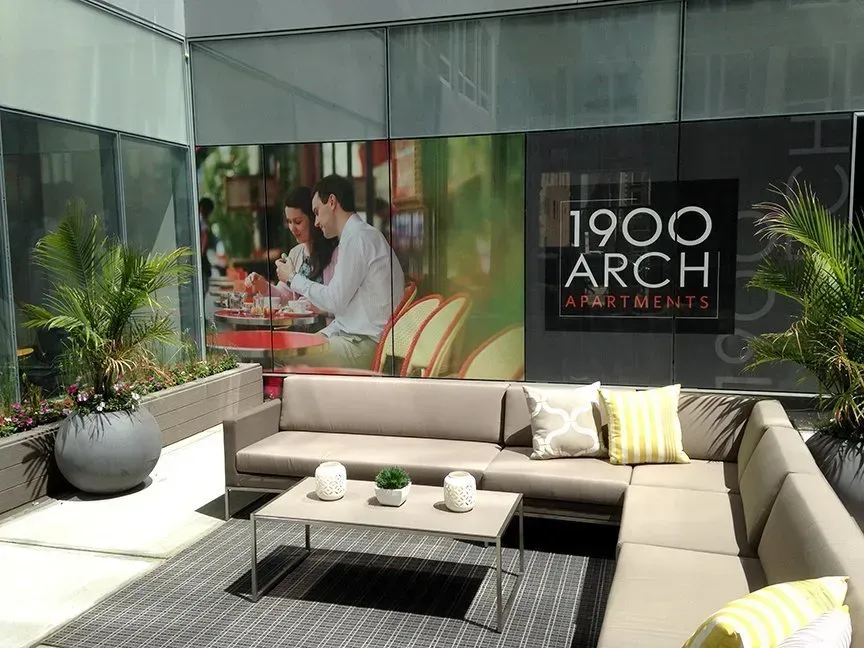 Outdoor lounge with beige sectional sofa, coffee table, potted plant, and 1900 ARCH event banner