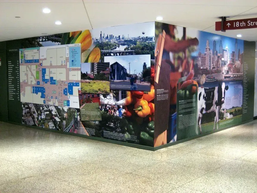 Colorful hallway mural with maps, city photos, and sports scenes on a dark wall display