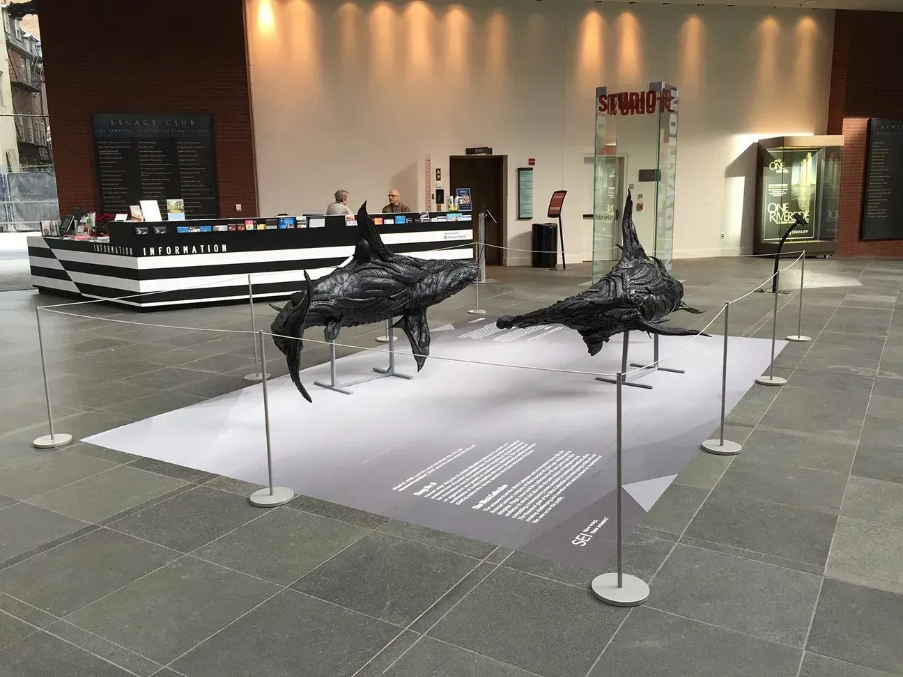 Museum display of two black metal animal sculptures on a white platform in a lobby