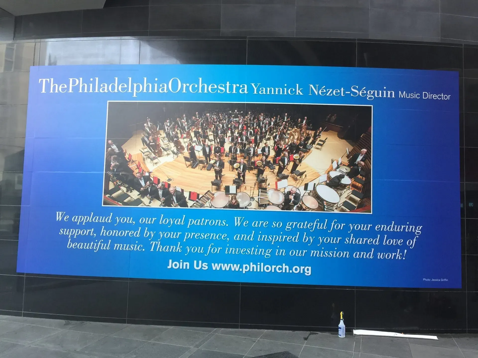 Blue Philadelphia Orchestra ad with a concert photo and white text on a screen at night