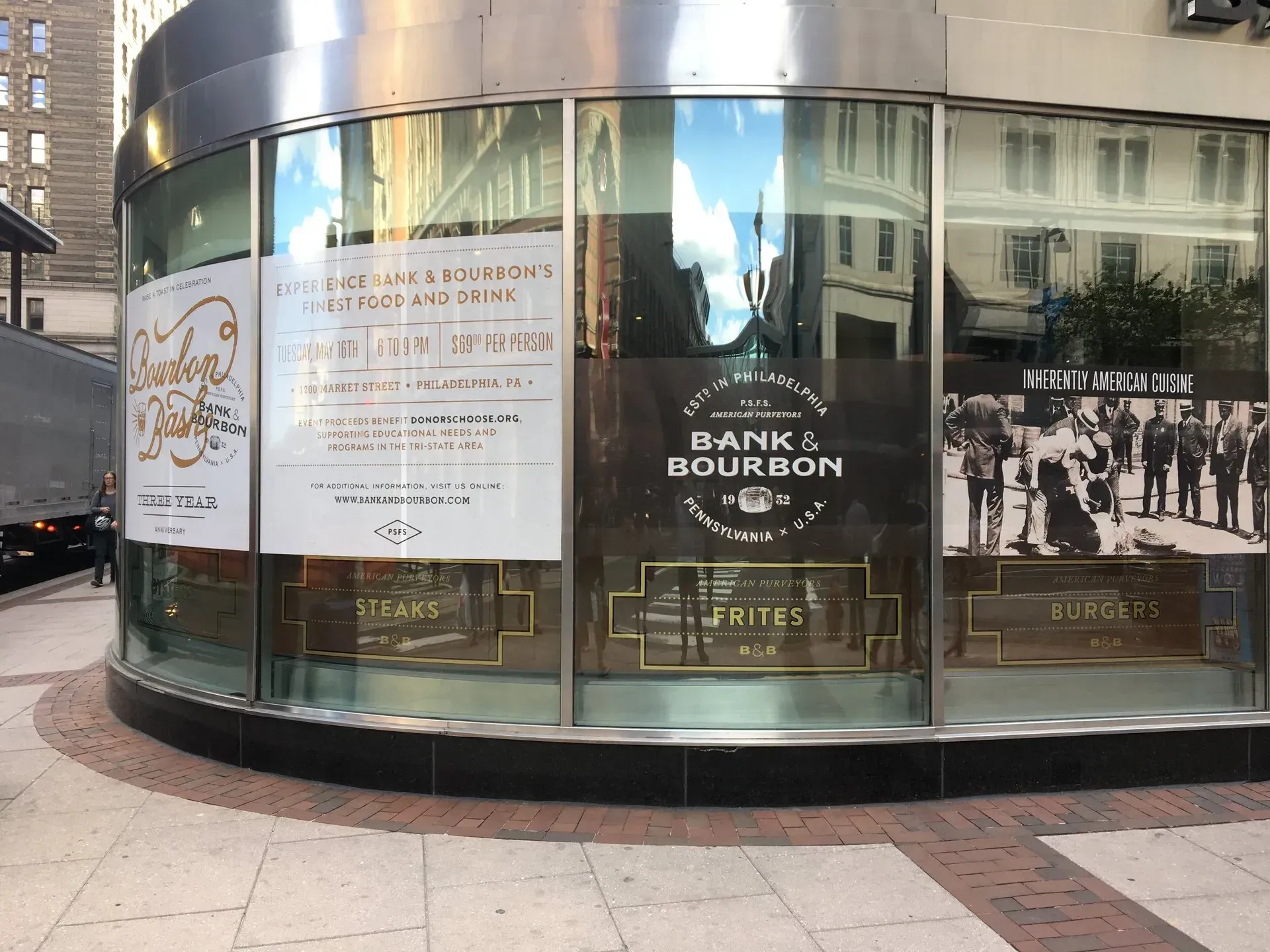 Storefront window display with posters, including a “Bank of Bourbon” sign and black-and-white crowd photo.