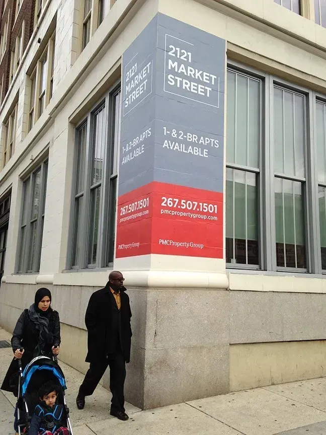 Sidewalk beside a building with a red-and-gray 212 Market Street sign; two pedestrians pass by.