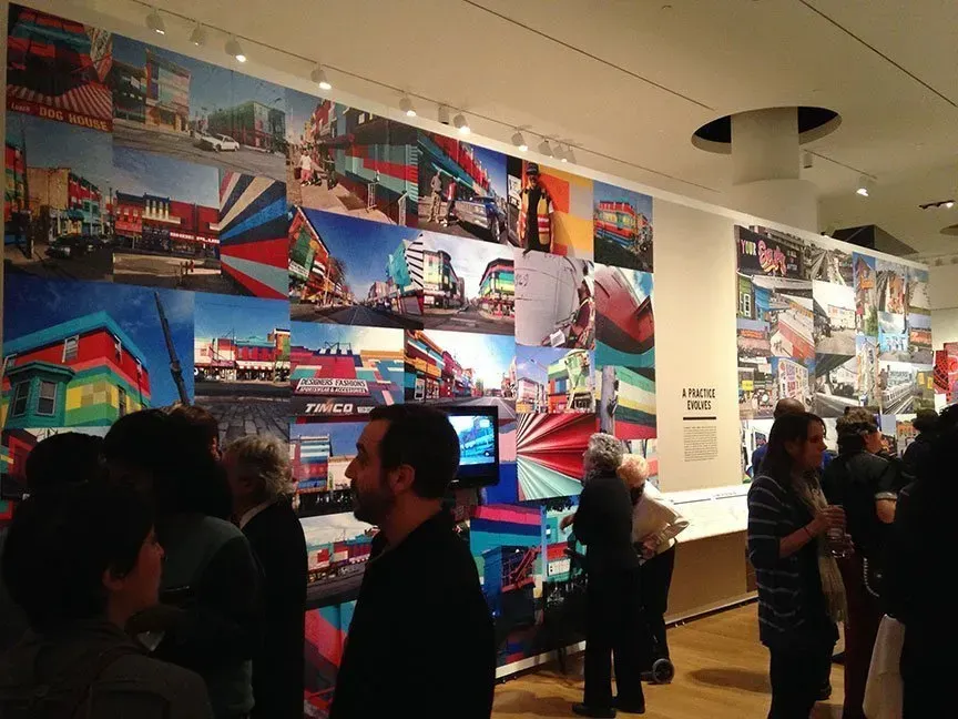 People browsing a colorful wall display in a gallery or museum interior.