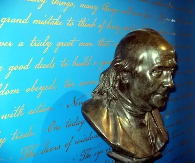 Bronze bust of Benjamin Franklin on a blue background with cursive writing