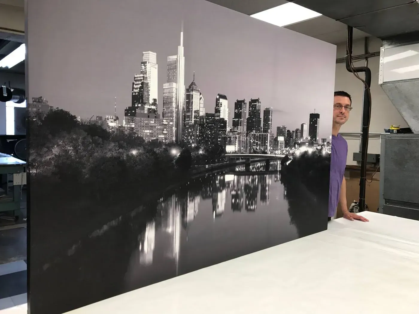 Black-and-white city skyline mural on a wall, with a man peeking from behind it in a workshop.