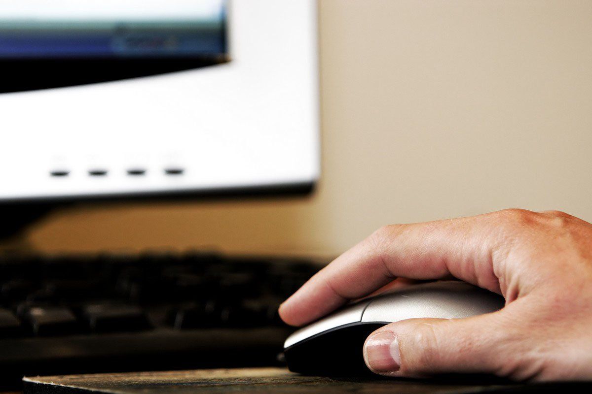 Hand using a computer mouse beside a monitor and keyboard on a desk