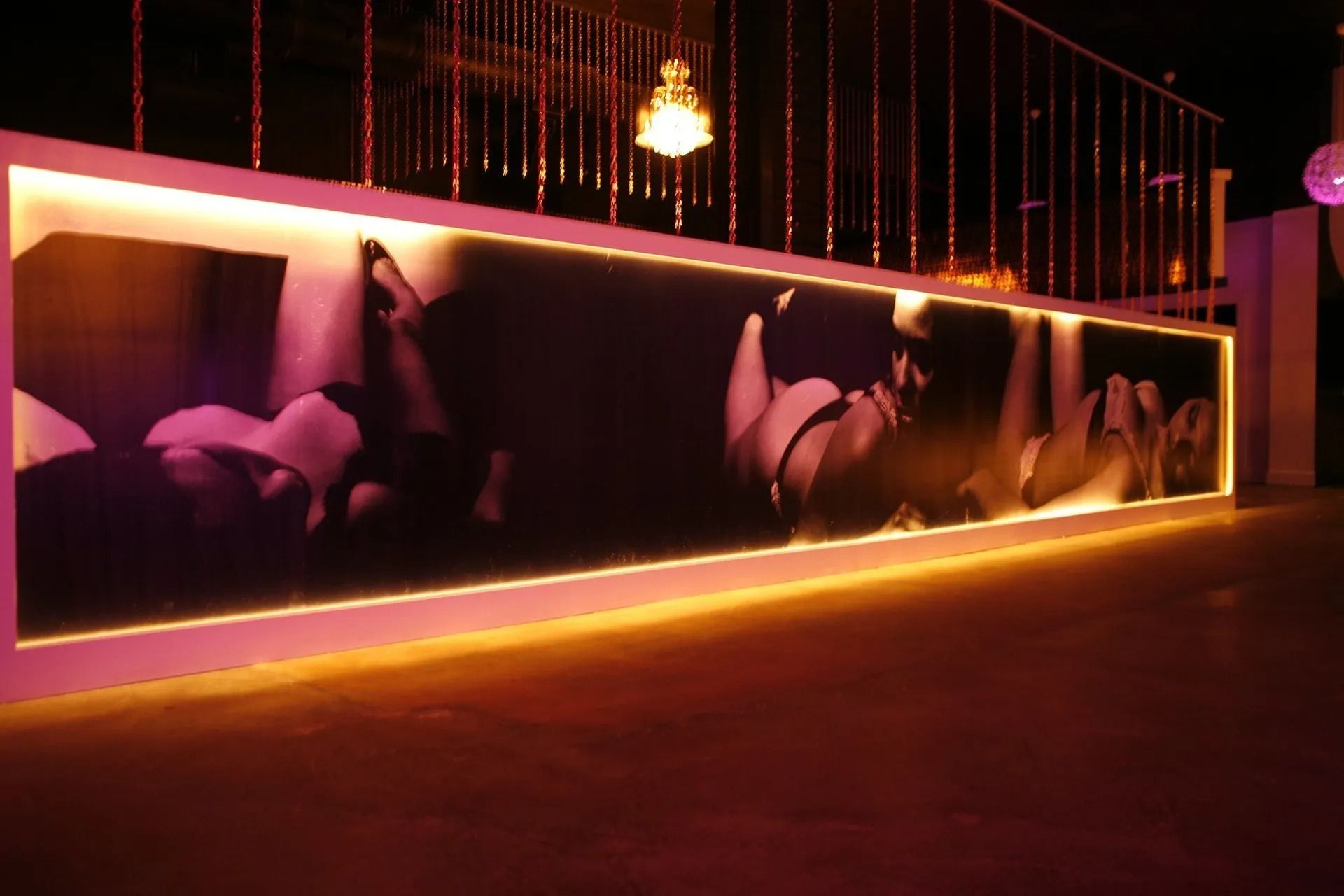 Neon-lit wall mural of large flowers in a dark indoor hallway with warm orange lighting