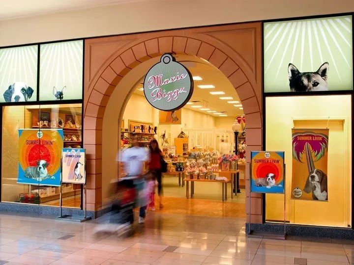 Mall storefront with circular arch entrance, colorful posters, and a blurred shopper passing by