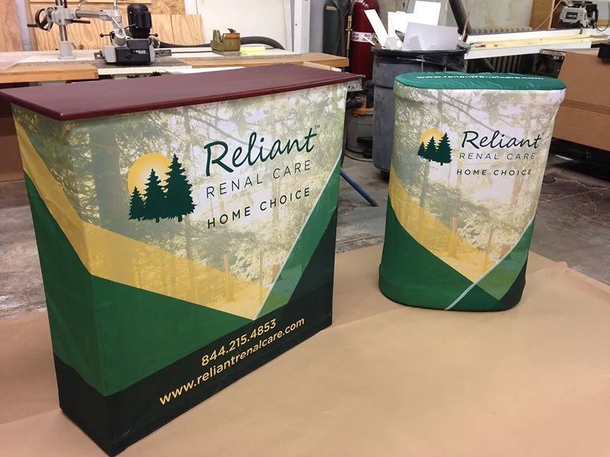 Two Reliant-branded booth display stands in green, yellow, and white on a table