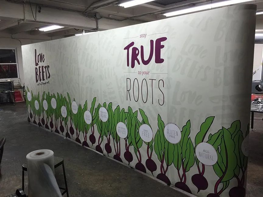 Mural reading “TRUE ROOTS” with painted green plants and purple roots along a wall in a garage-like space