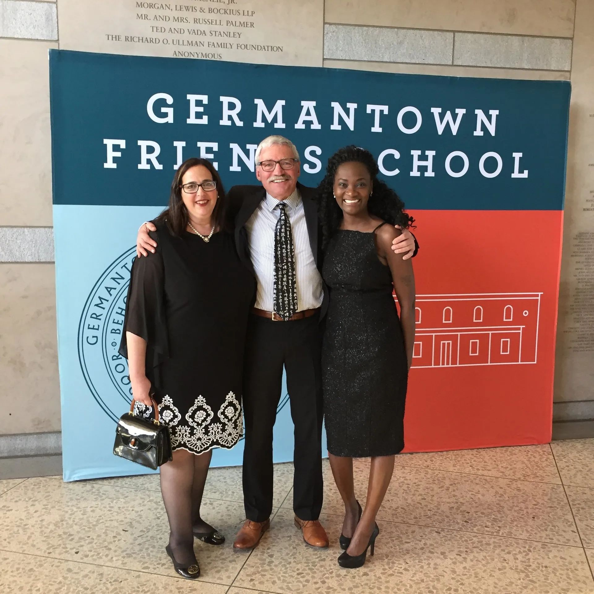 Three people posing in front of a Germantown Friends School banner at an event.