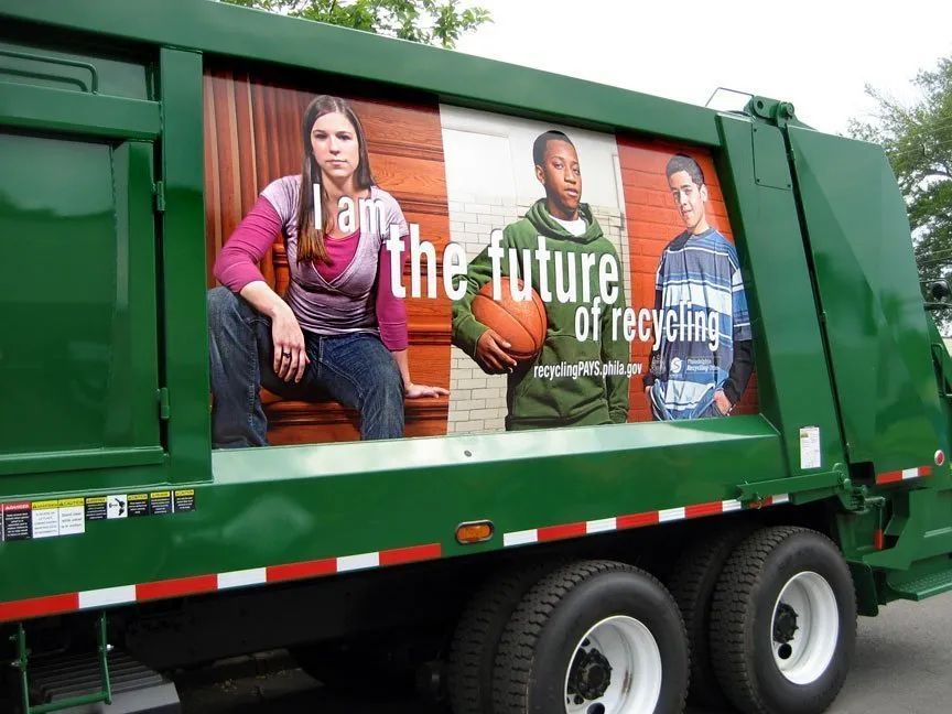 Green recycling truck with a side ad showing three seated people and the text “the future of recycling”