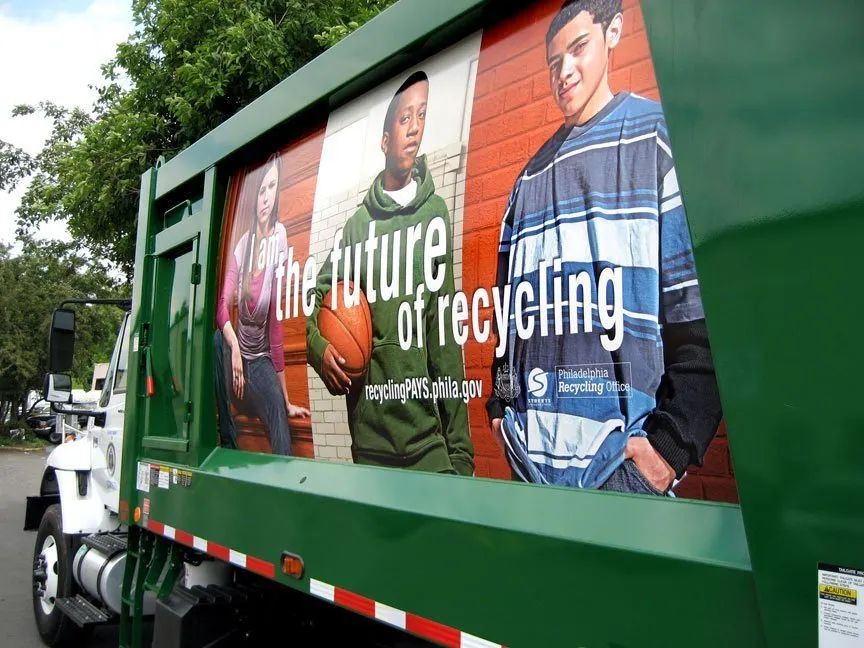 Green recycling truck with a large ad reading “The future of recycling” and two people holding recycling items