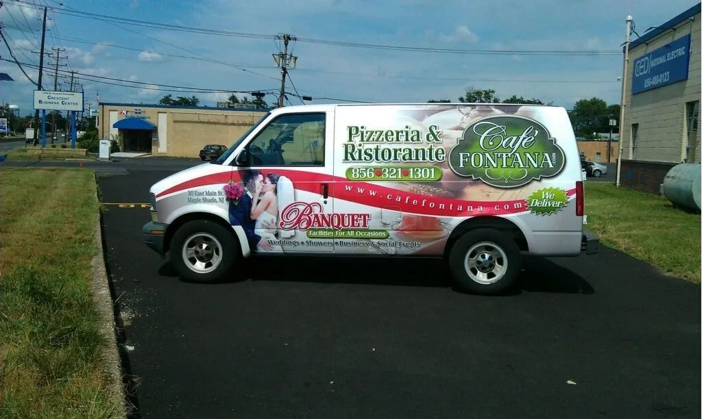 White catering van with “Pizzeria & Rostorante” signage parked in a lot.