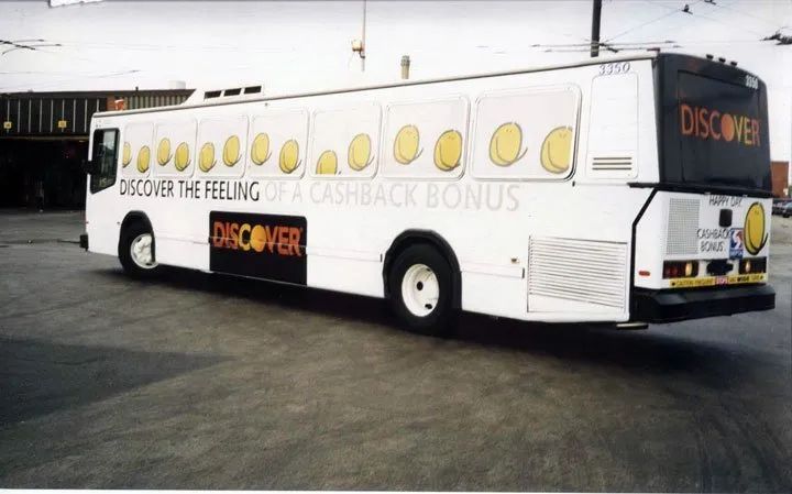 White bus with yellow circle graphics and “DISCOVER” signage parked in a lot