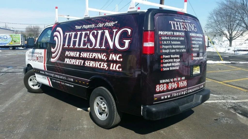 Black service van with THIESING roofing and exterior services branding parked in a lot on a sunny day