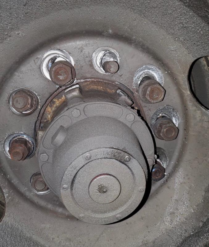 A close-up view of a vehicle wheel hub showing several rusty lug nuts, including one missing nut on the wheel rim.