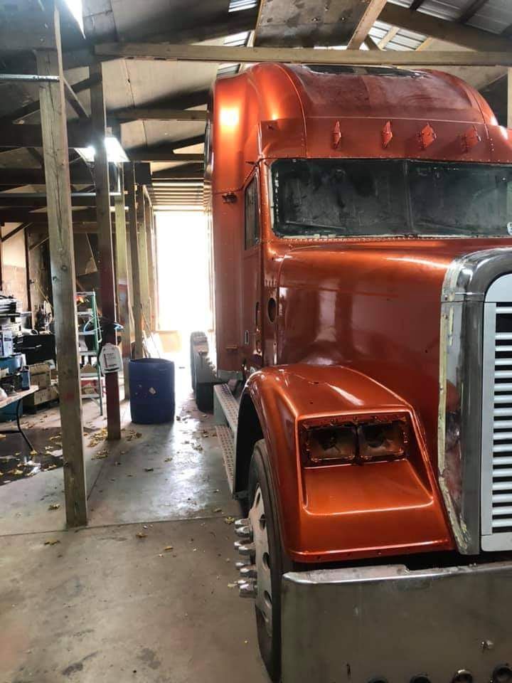 A metallic orange semi-truck cab parked inside a dimly lit workshop.