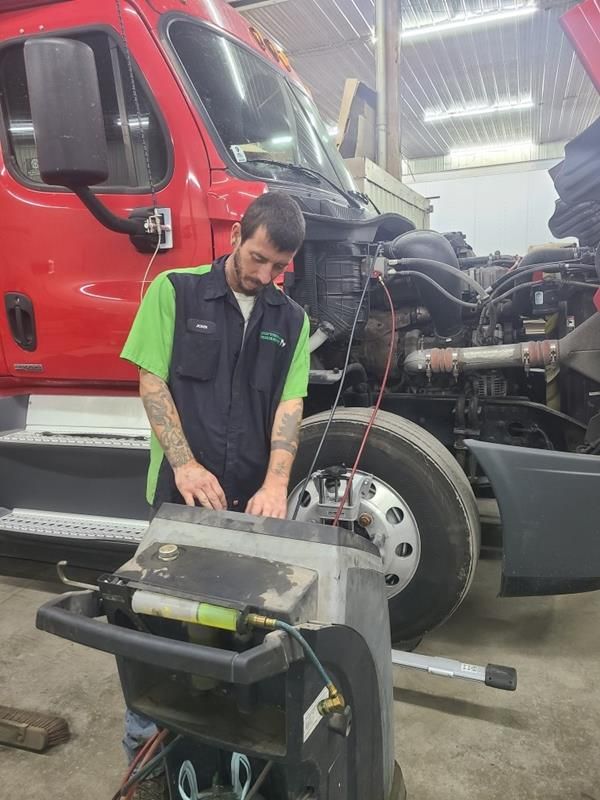 A mechanic in a green and black uniform uses diagnostic equipment on a red truck inside a repair shop.