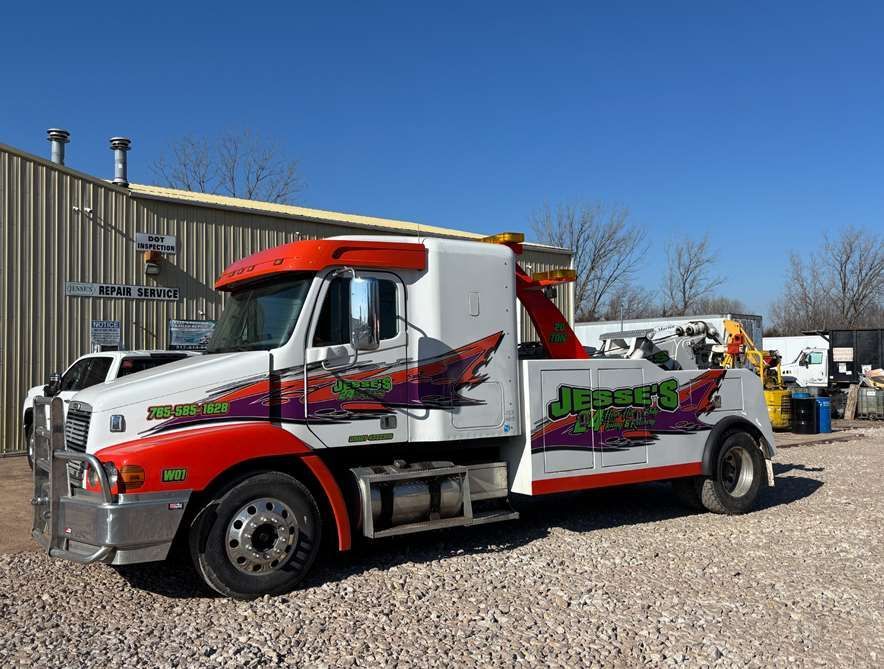 A white and red Jesse’s Towing truck parked on a gravel lot under a clear blue sky.