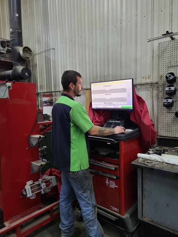 A technician in a green and black uniform uses a computer at a red diagnostic workstation in an automotive repair shop.