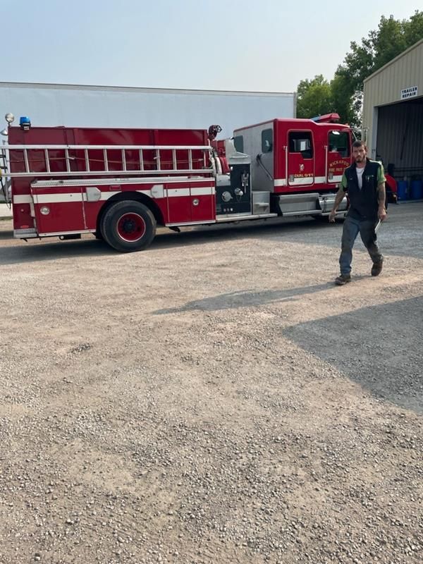 A red fire truck parked on a gravel lot near a building as a person walks toward the camera.