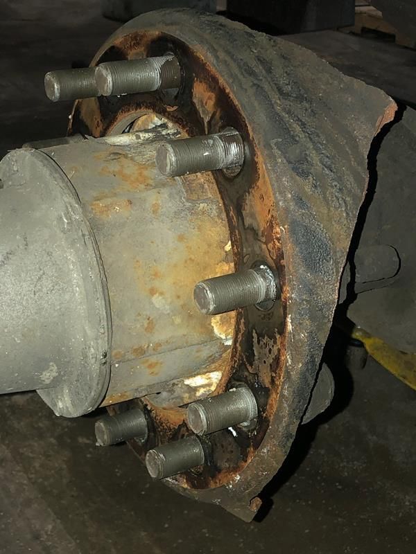 A rusty, heavy-duty vehicle wheel hub assembly with multiple exposed mounting studs and a damaged brake drum backing plate.