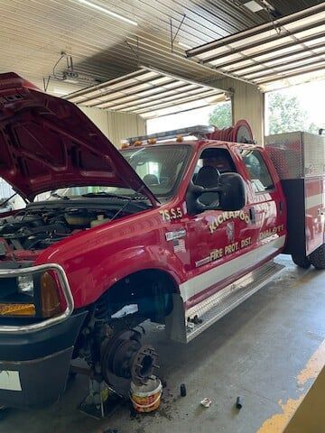 A red fire truck with its hood open and front tire removed is parked inside a garage for maintenance.