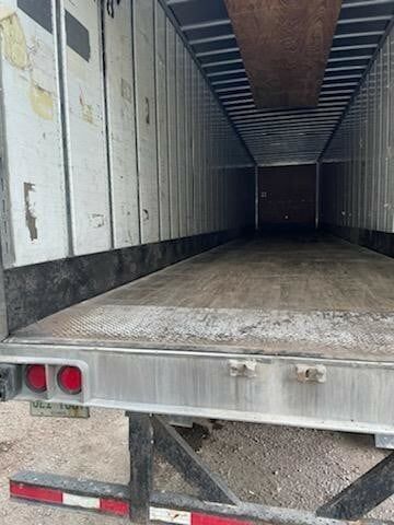 The open rear view of an empty semi-trailer truck with wood flooring, white side panels, and metal rear bumper.