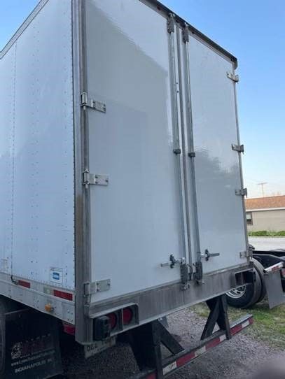 A close-up view of the rear white swing doors and metal hardware of a semi-trailer parked outdoors.
