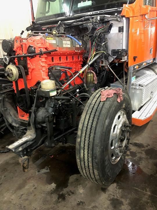 A bright orange semi-truck engine exposed in a workshop, with a large front tire visible in the foreground.