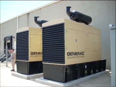 Two large beige Generac industrial generators outside a building on a concrete pad