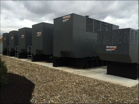 Rows of large black industrial generators or battery units on a gravel lot under a cloudy sky