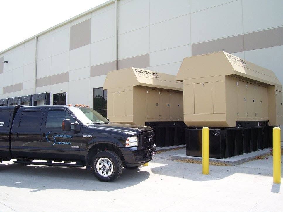 Black pickup truck parked beside beige industrial equipment with yellow bollards in a snowy lot
