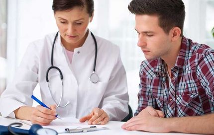 Doctor writing on a form while consulting with a patient in an office.