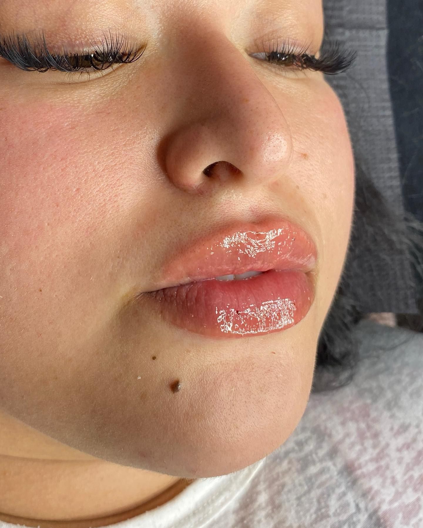 A close-up view of lips with a glossy, light pink finish, showing the texture and shine of the lip product applied.