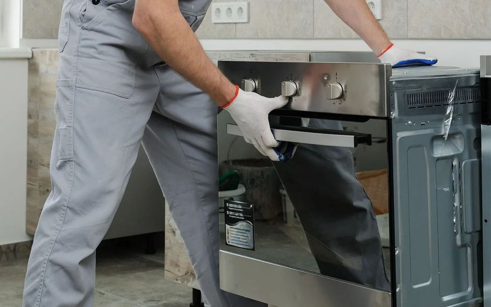 Person wearing work gloves installing a stainless steel oven in a kitchen.