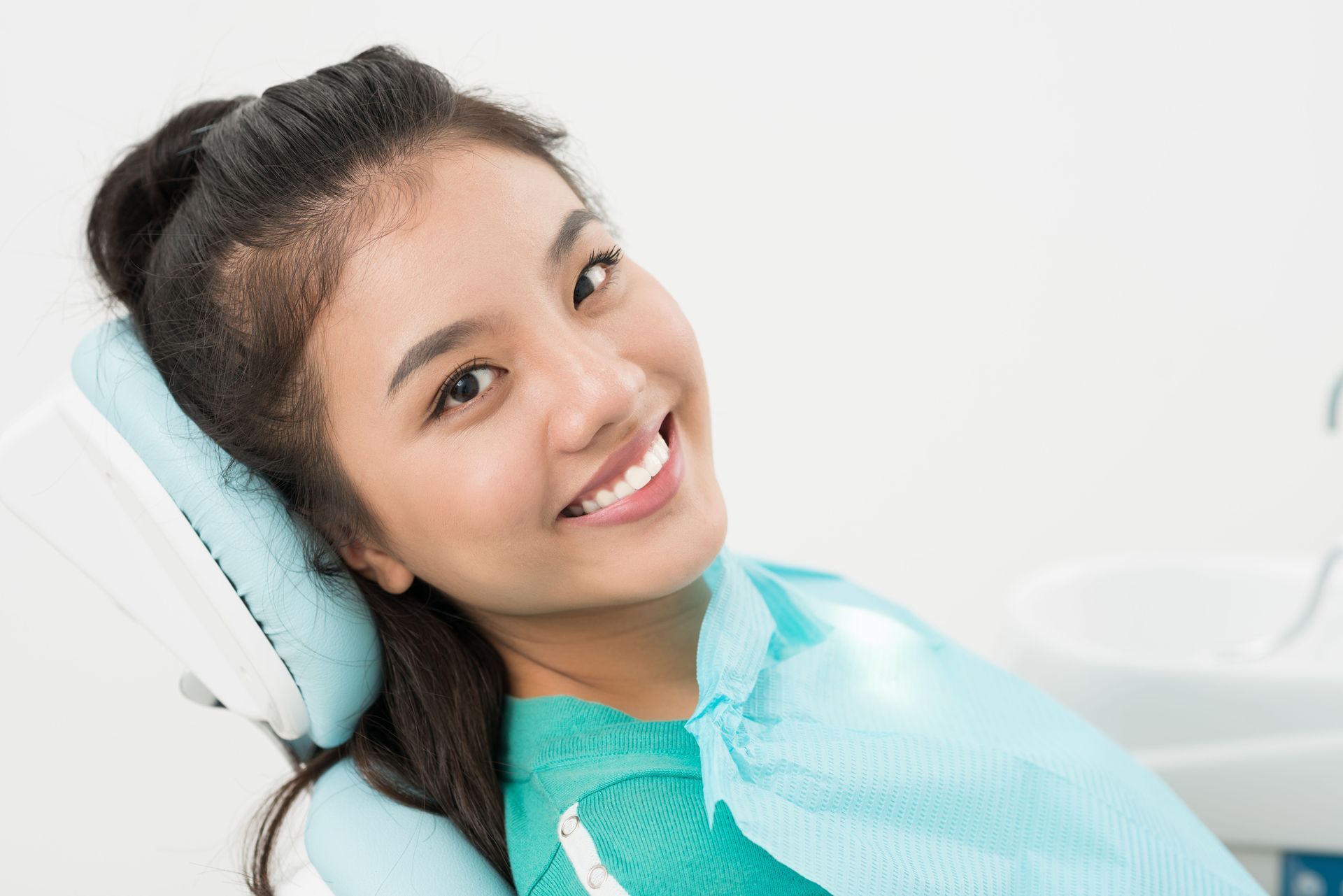 Woman smiling in a dentist's chair, wearing a bib, in a dental office.