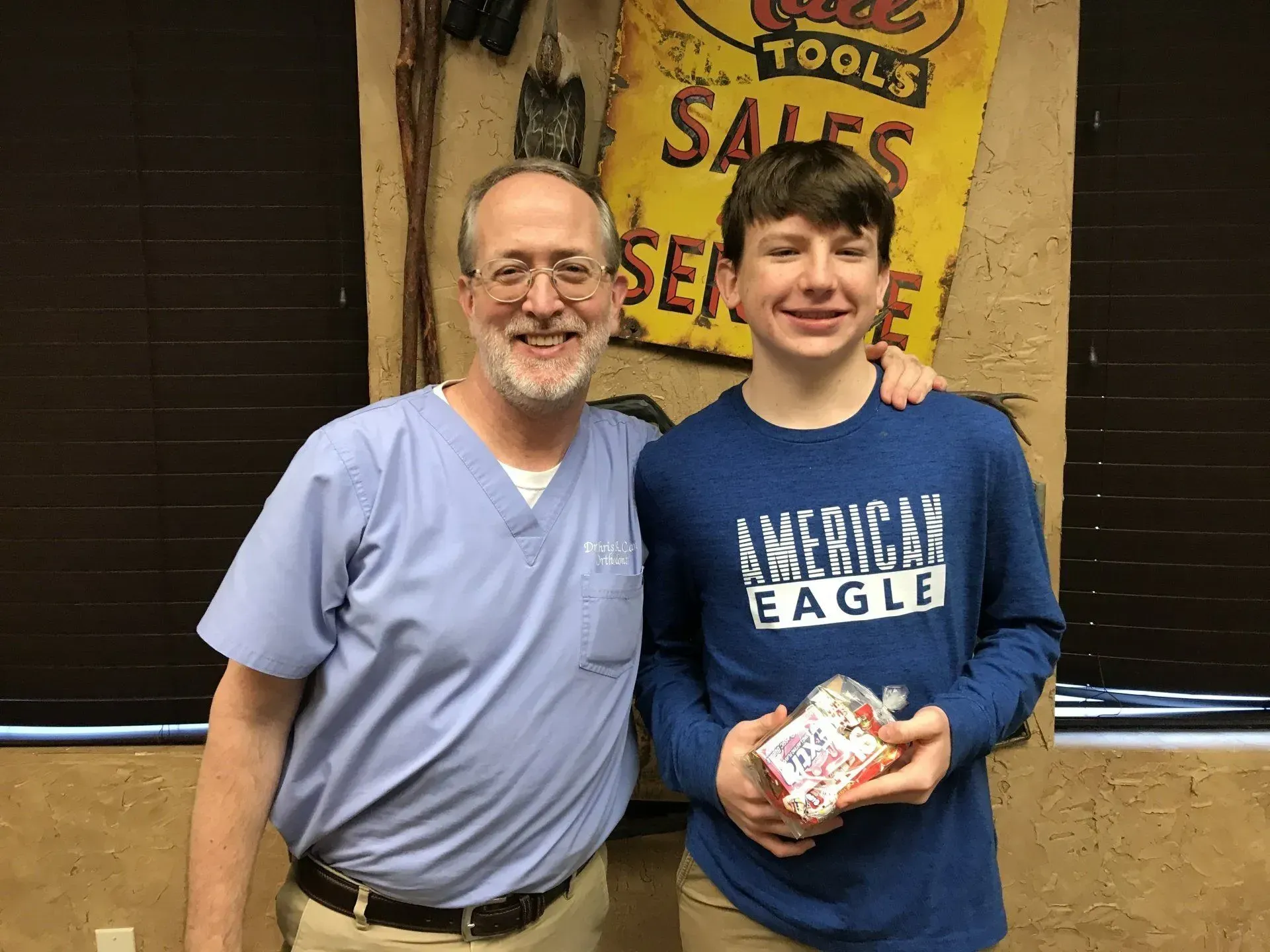 Man in scrubs with a younger person, both smiling, holding a gift; 