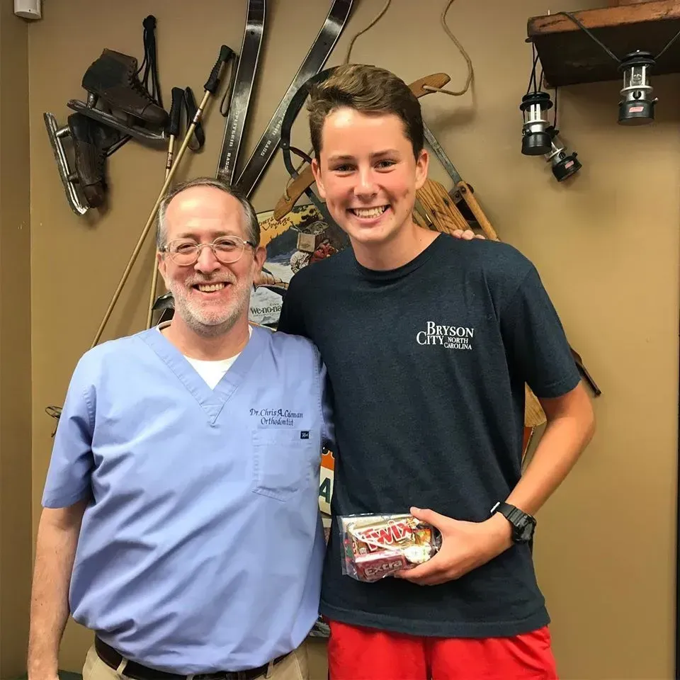 A man in scrubs and a teenager smile, posed with sporting equipment on wall.