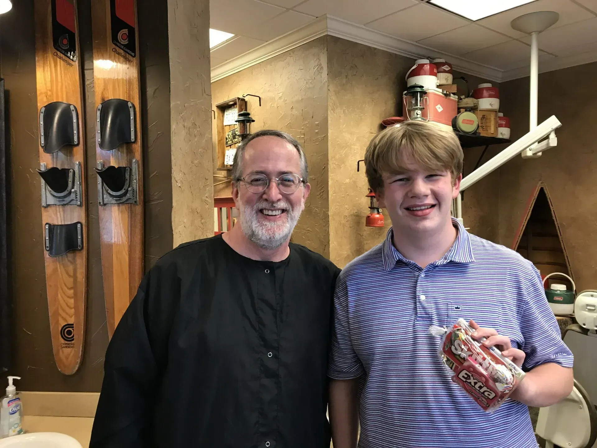 Man and teen smiling; teen holds a product, standing in a shop with water skis on the wall.
